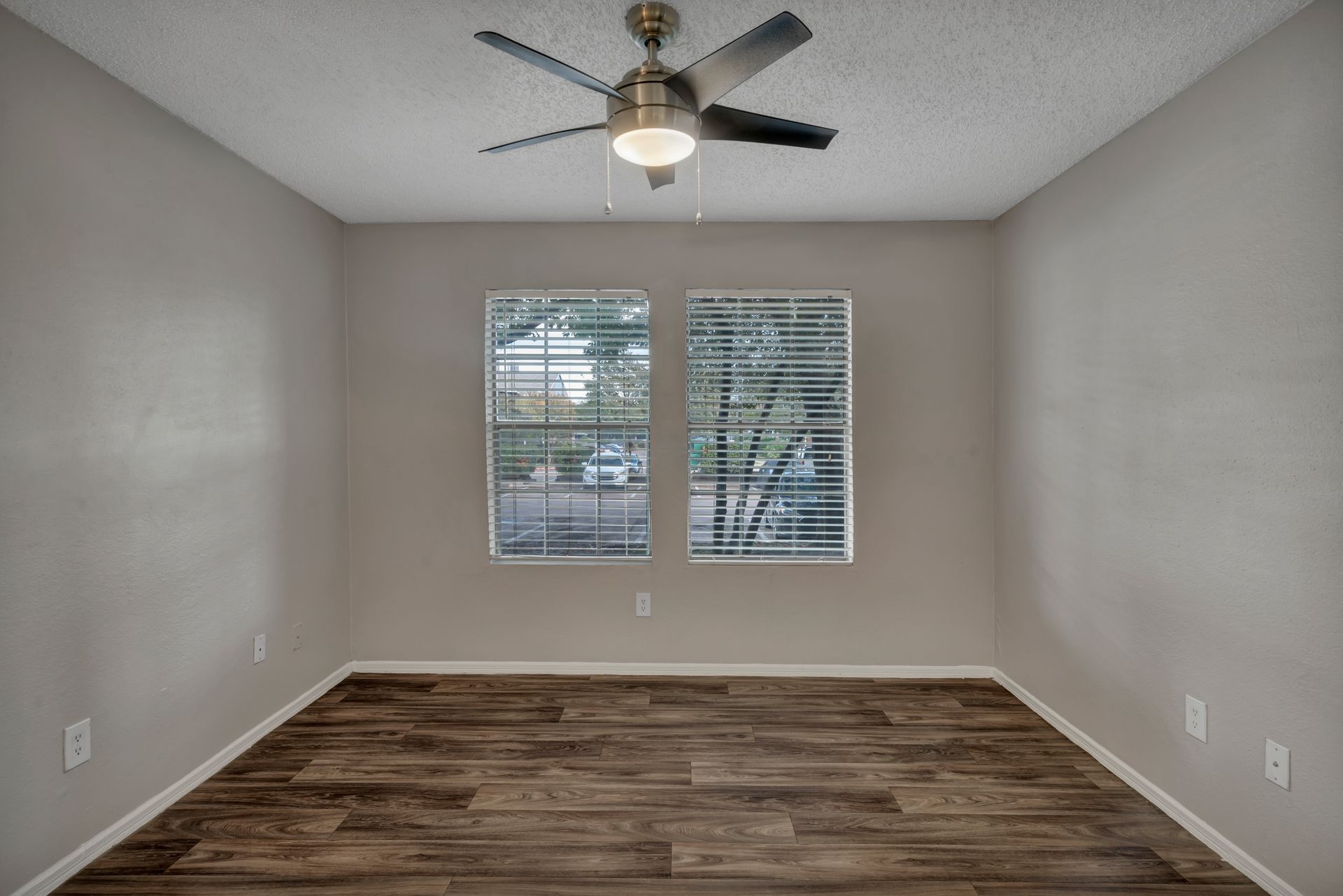 An empty room with a ceiling fan and two windows.