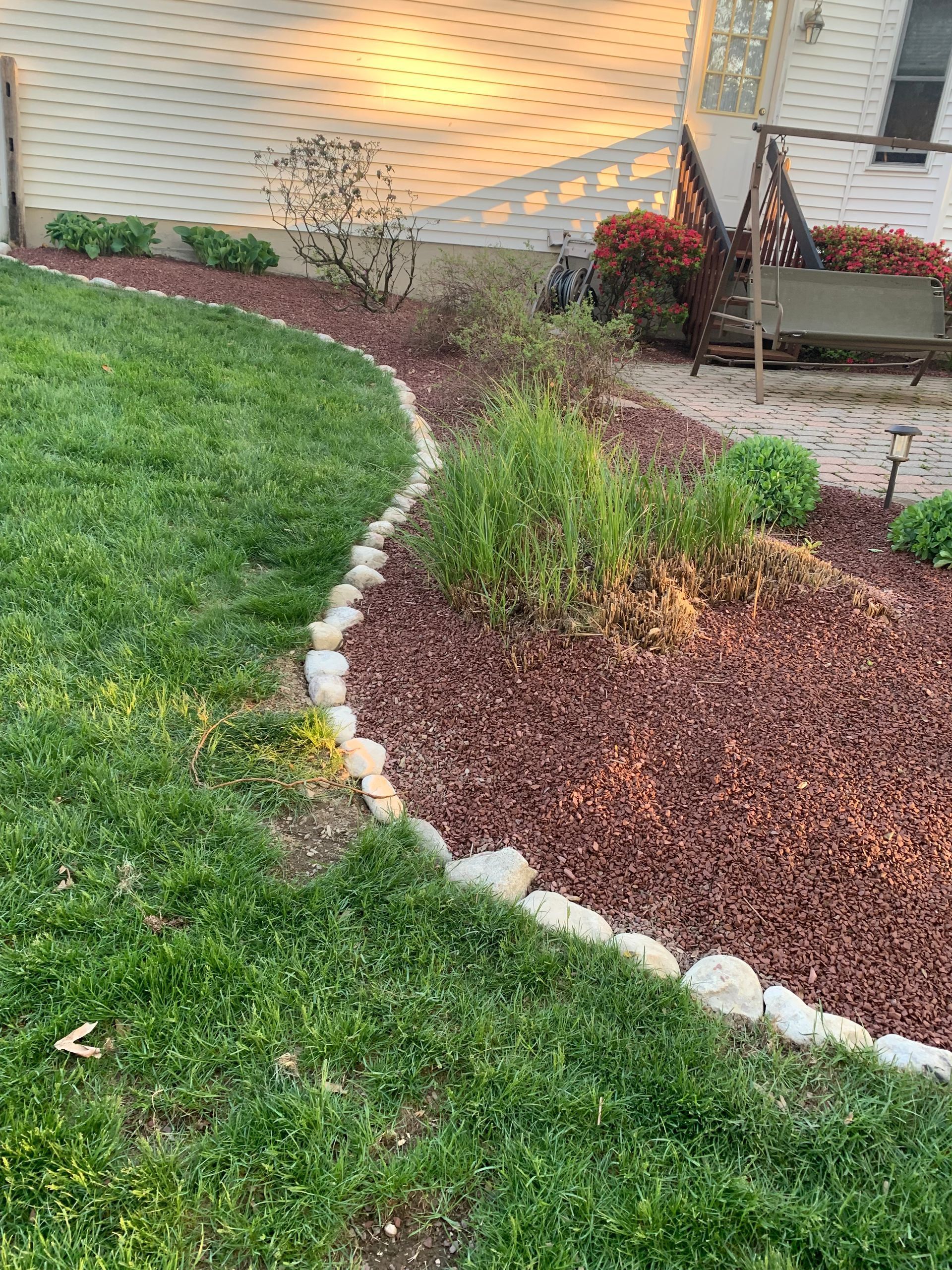 a lawn with a rock border and a swing in the background .