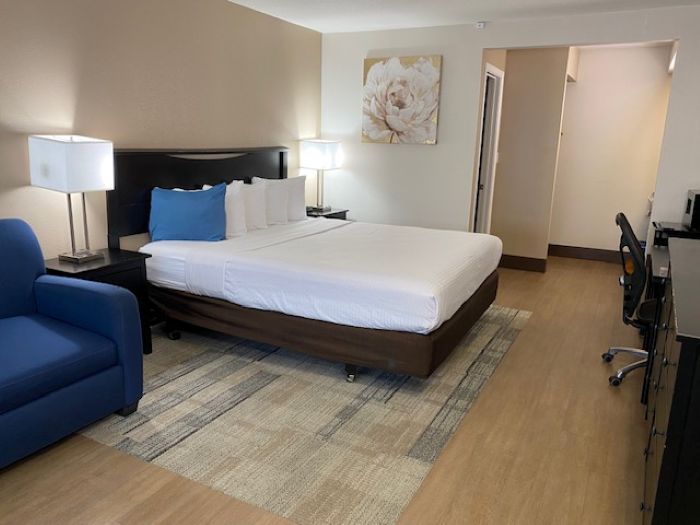 Hotel room with a king bed, blue chair, desk, and soft beige decor