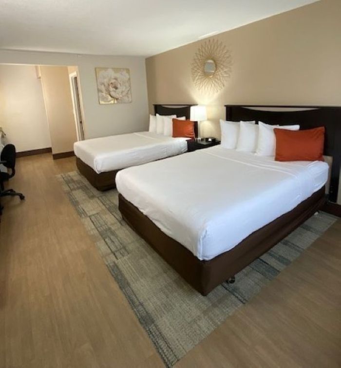 A hotel room with two beds, brown headboards, white bedding, and orange pillows.