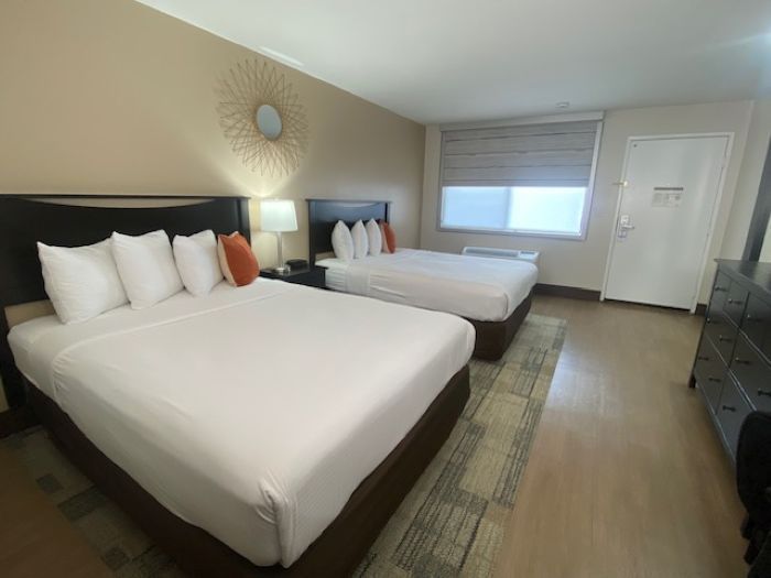 Hotel room with two made beds, beige walls, a window, and a dresser.