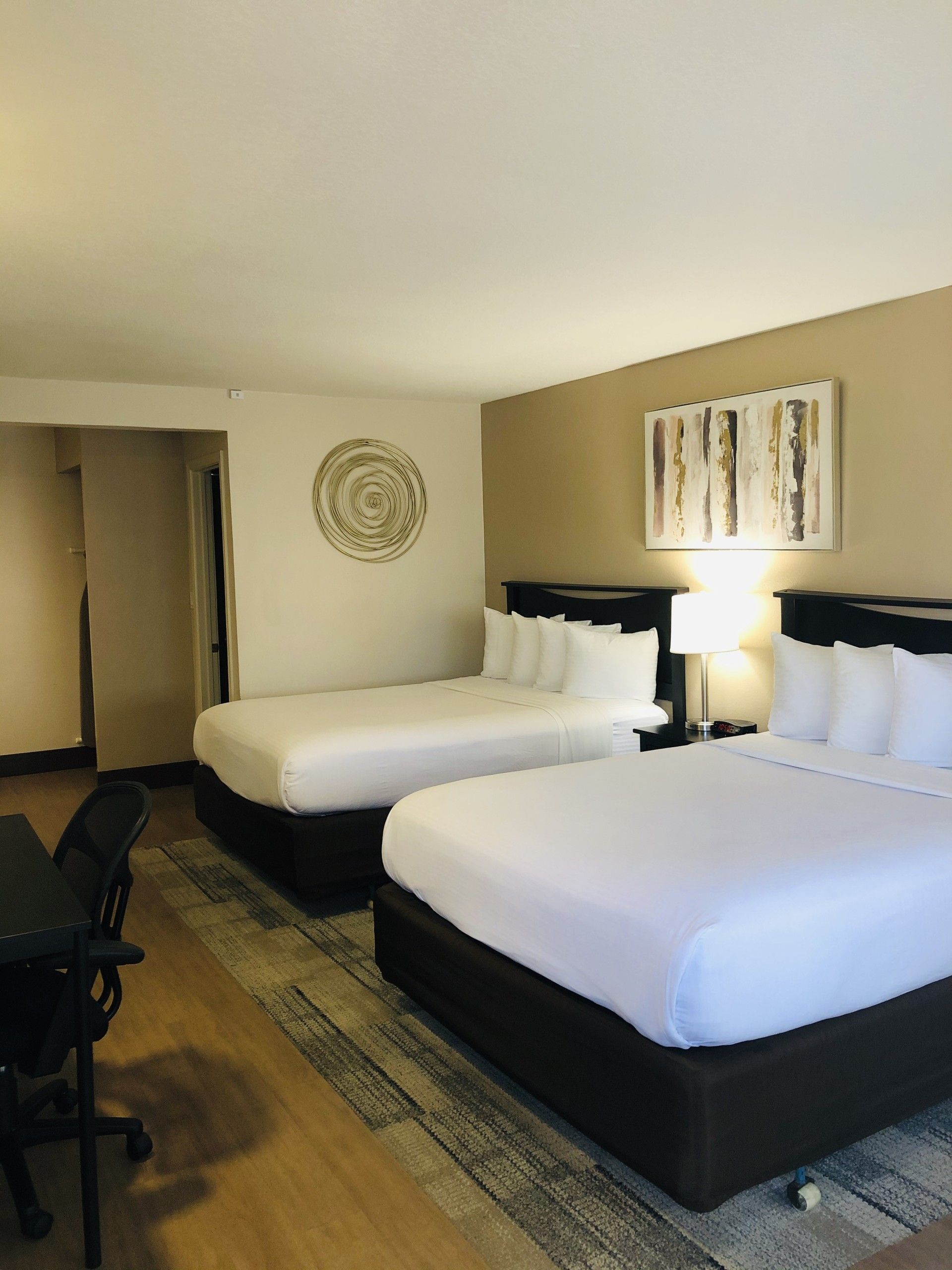 Hotel room with two queen beds, bedside lamps, a desk chair, and beige walls.