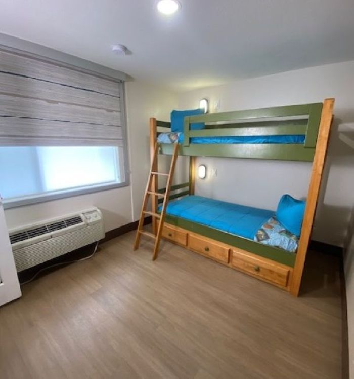Small bedroom with a wooden bunk bed, blue bedding, ladder, window, and air conditioner.