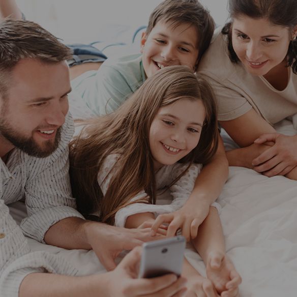 Family gathered on a bed, smiling while looking at a smartphone together