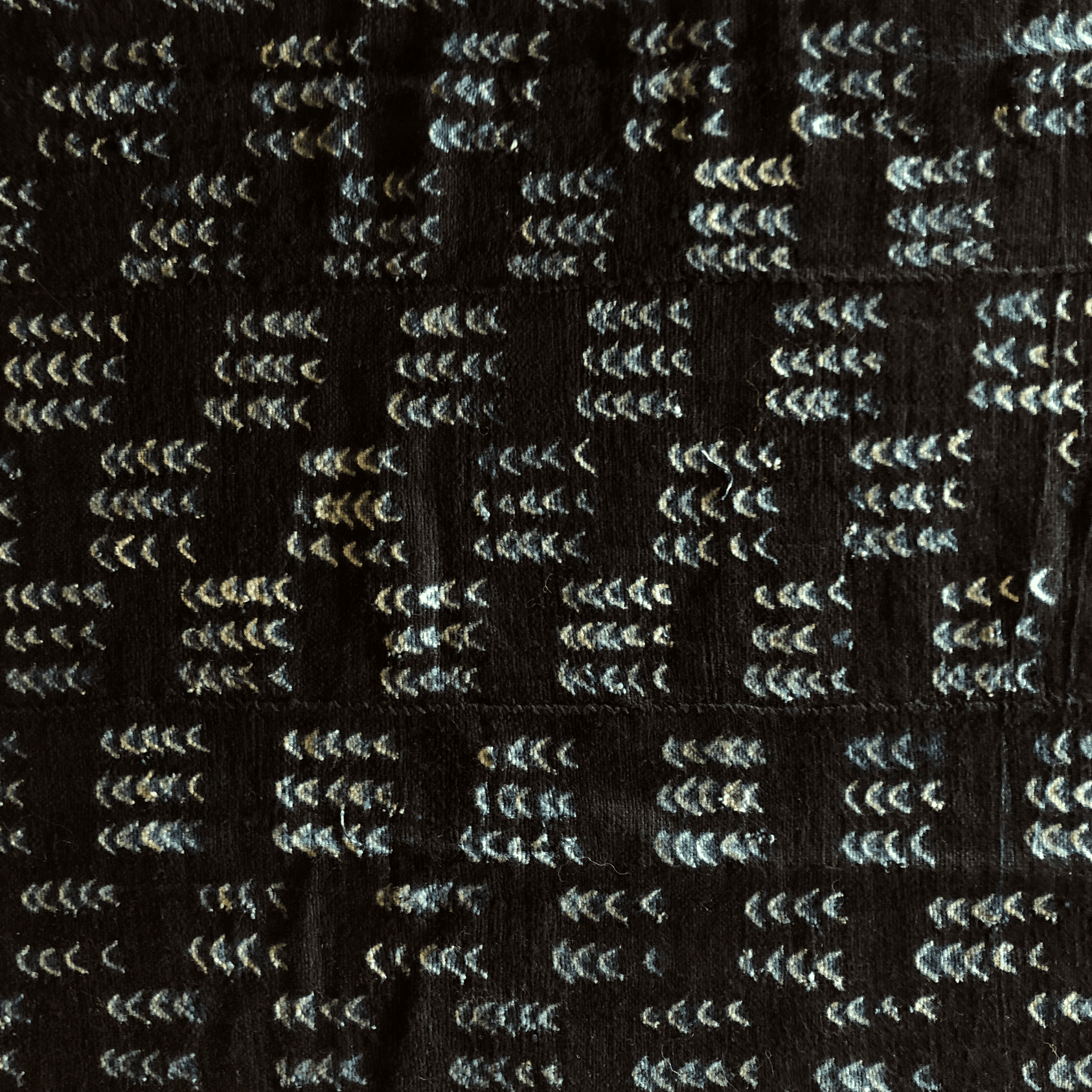 Tissu foncé avec des rangées répétées de motifs blancs en forme de chevrons.