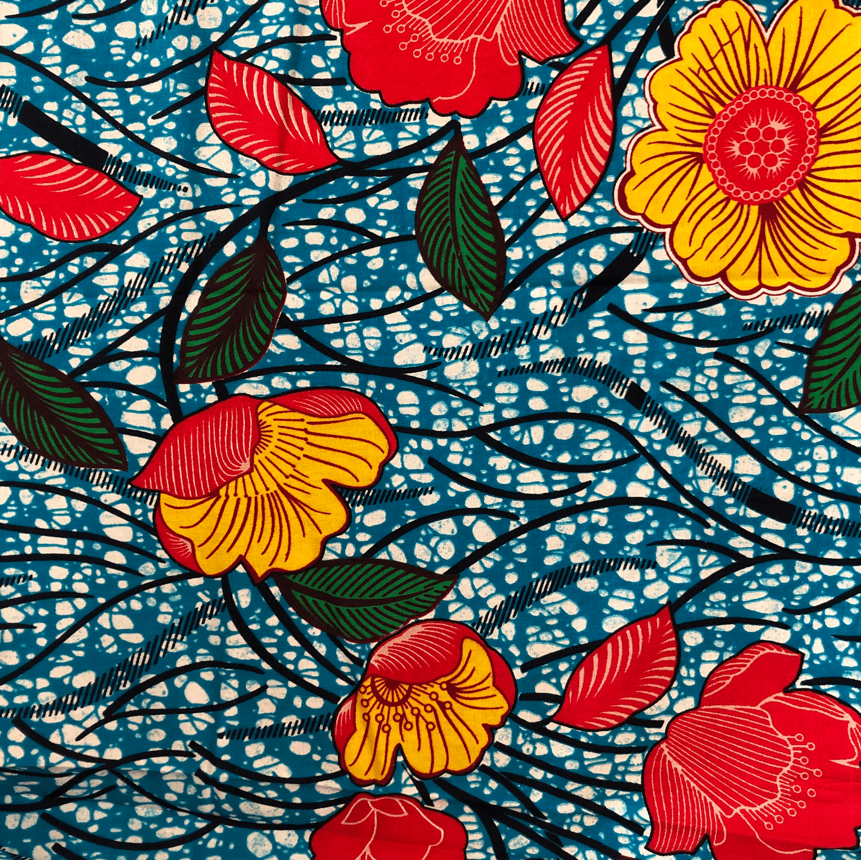 Tissu fleuri lumineux : fleurs jaunes et rouges avec feuilles vertes sur fond bleu moucheté.