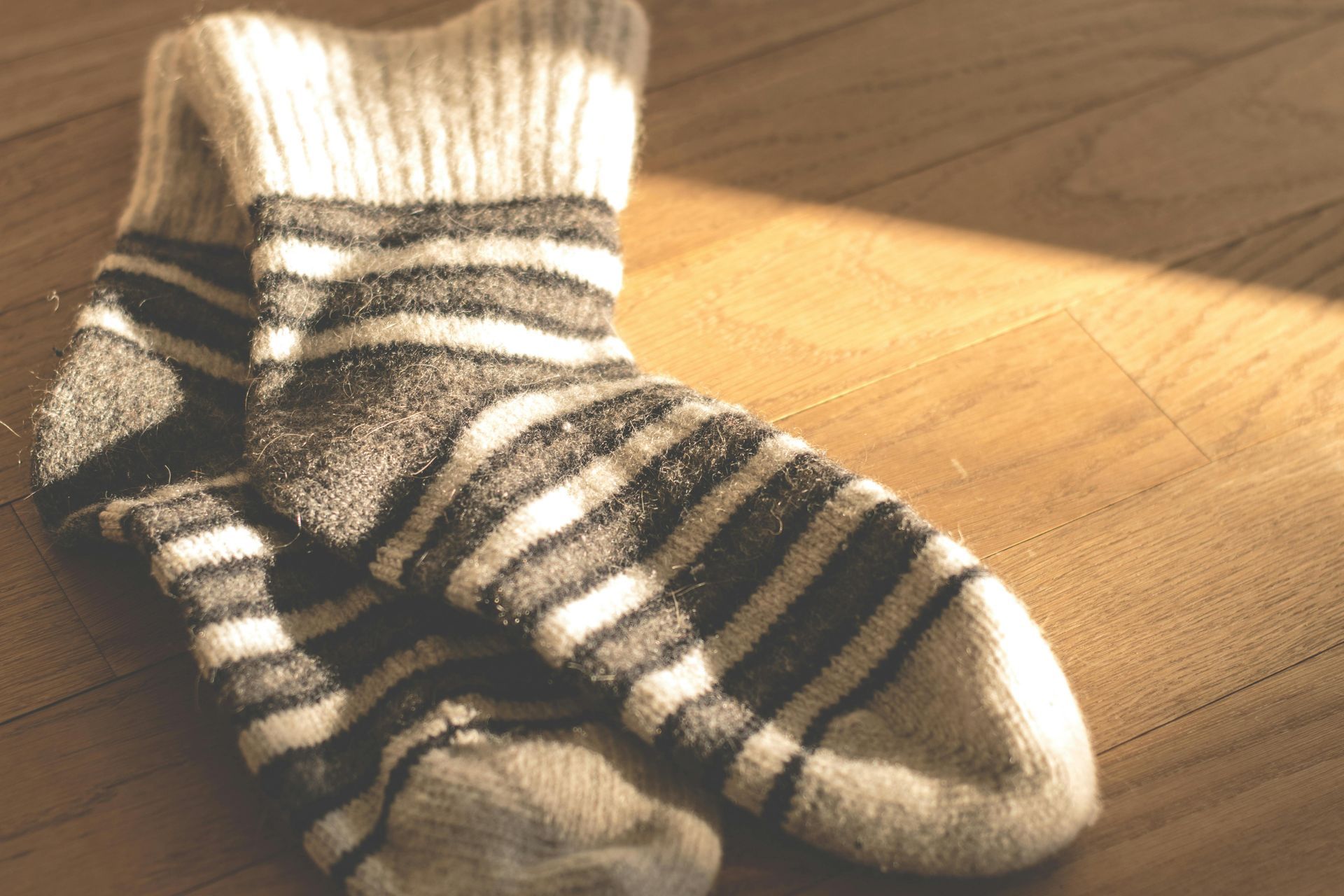 Des chaussettes en laine rayées sur un parquet, éclairées par la lumière du soleil.