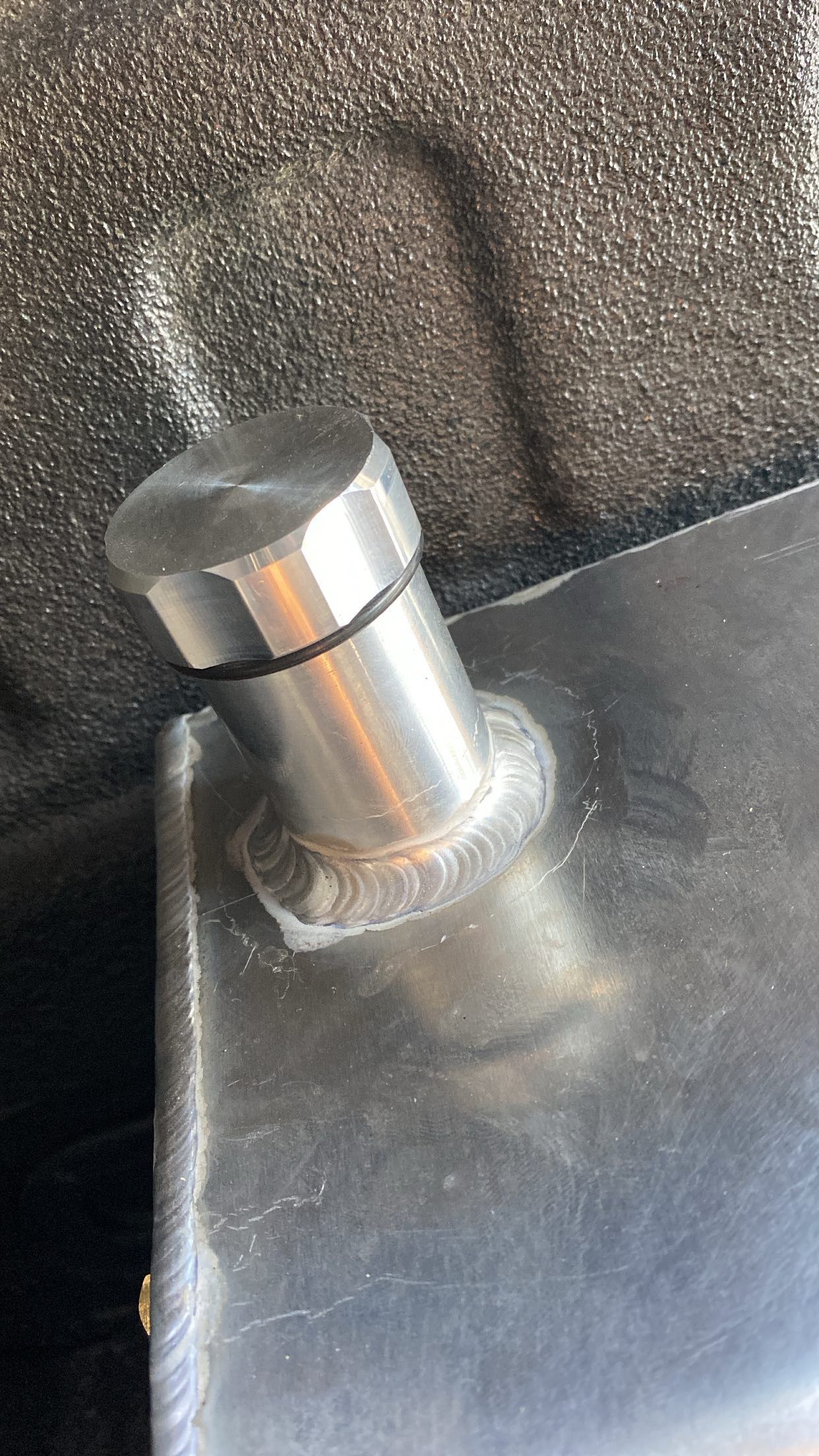 A close-up shot of a silver metal mounting pin welded onto an aluminum tank surface with a thin black O-ring.