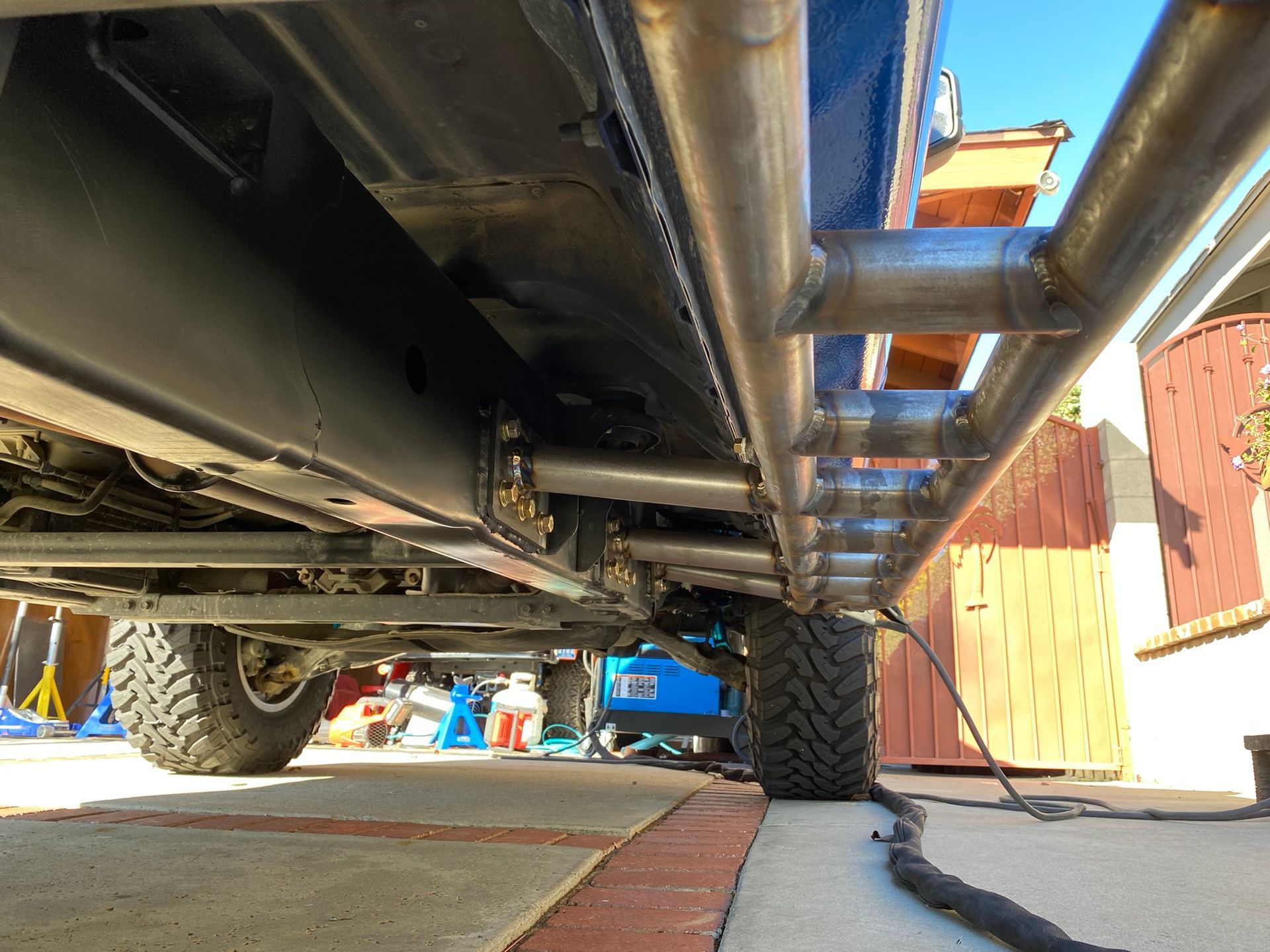 A low-angle view looking under a vehicle, showing a newly installed, custom welded metal rock slider attached to the frame.