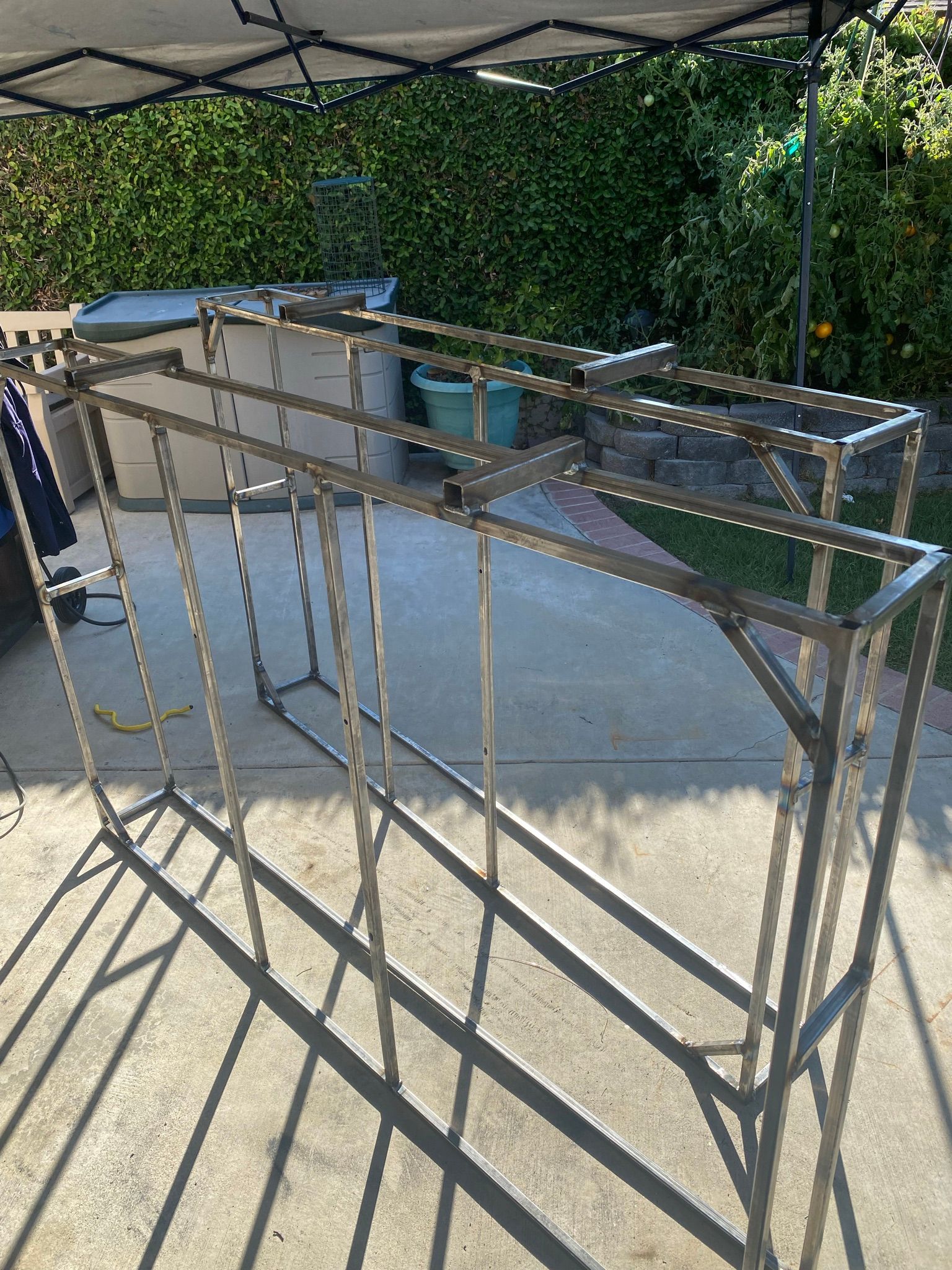 A metal rectangular frame structure stands on a concrete patio, likely a base for an aquarium or shelving unit.