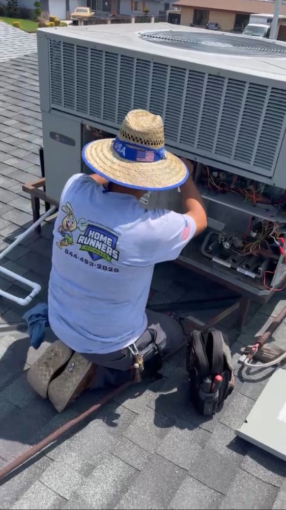 HVAC technician repairing rooftop air conditioner, wearing a hat and working on electrical components.
