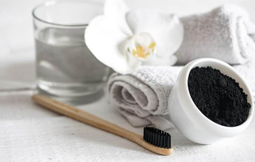 Toothbrush, charcoal powder bowl, towels, glass of water, and flower on a spa-like surface
