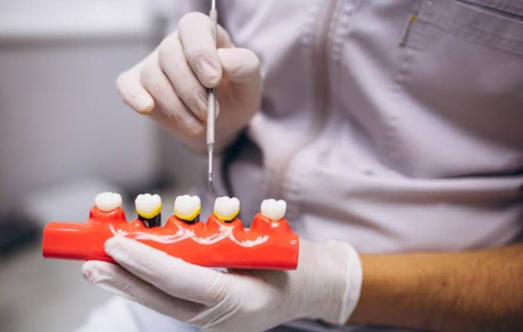 Dentist shaping a red dental model with tools, wearing gloves in a clinical setting