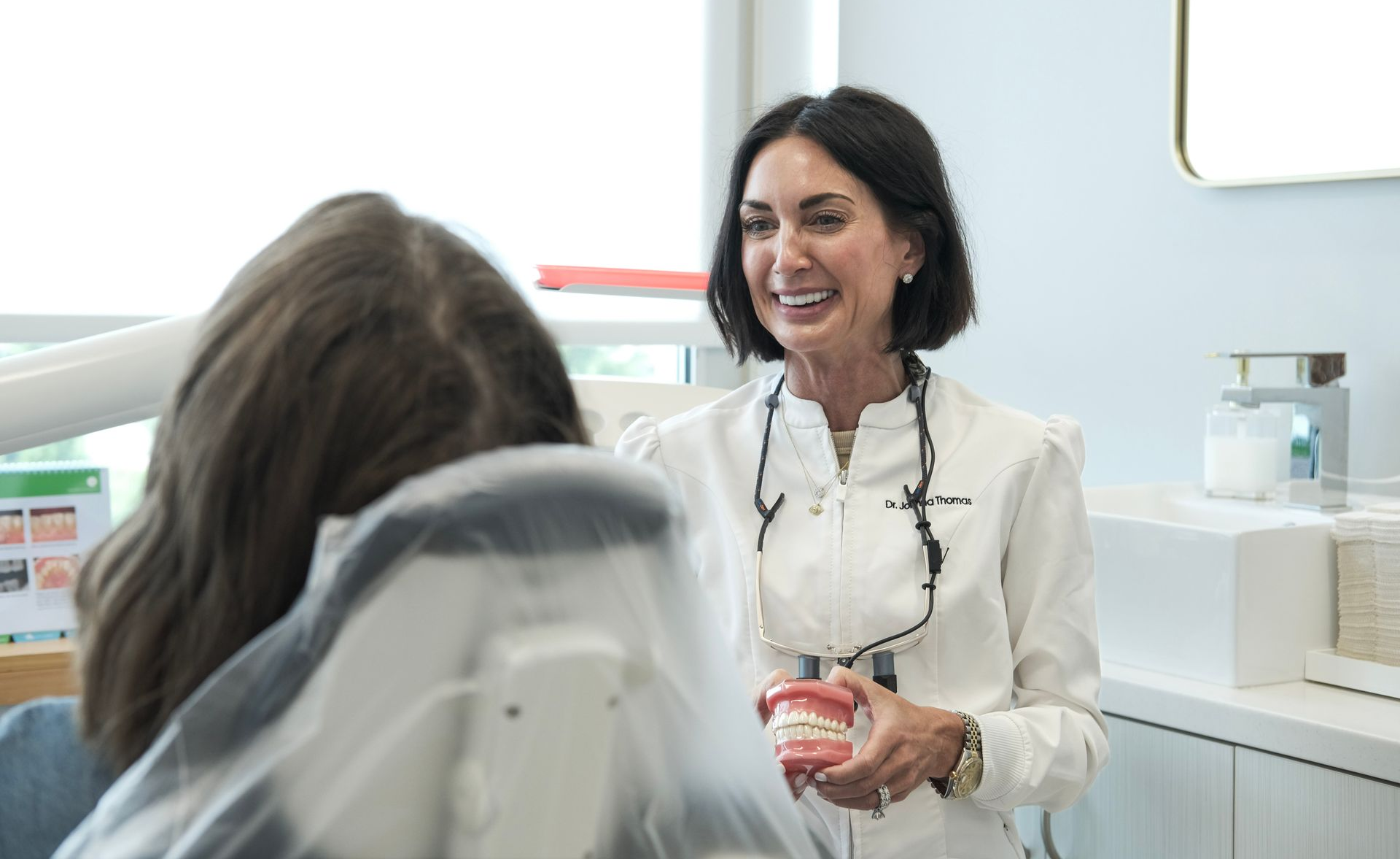 Smiling person in a white robe adjusting hair in a bathroom mirror