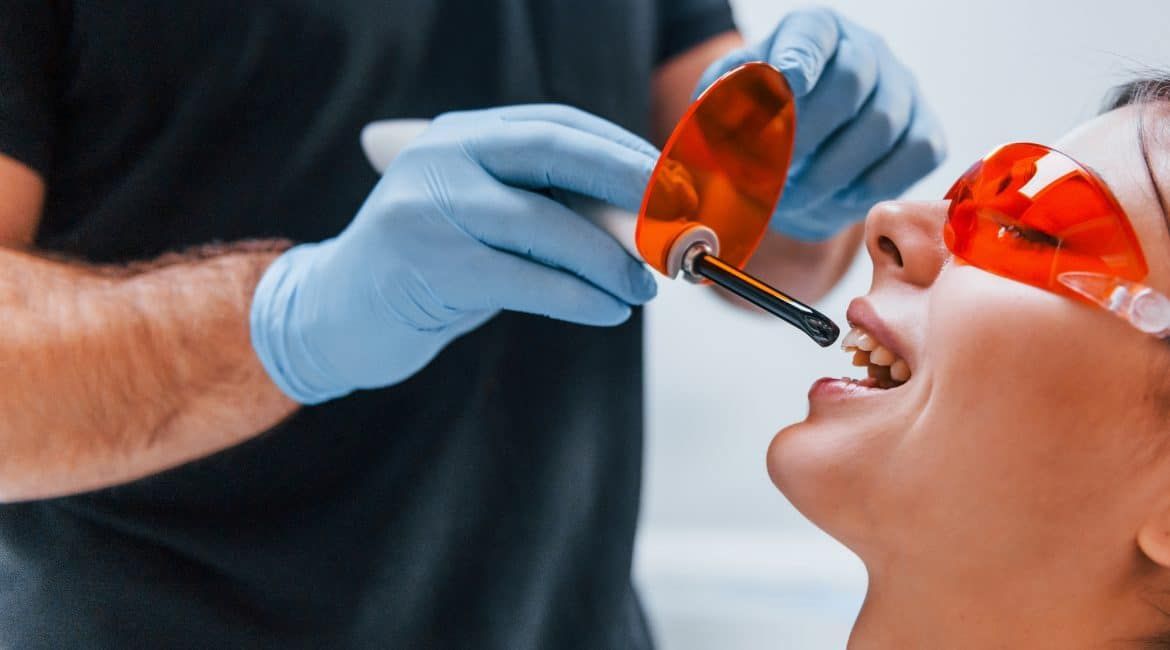 Dentist using a tool on a patient wearing orange safety glasses during a dental procedure