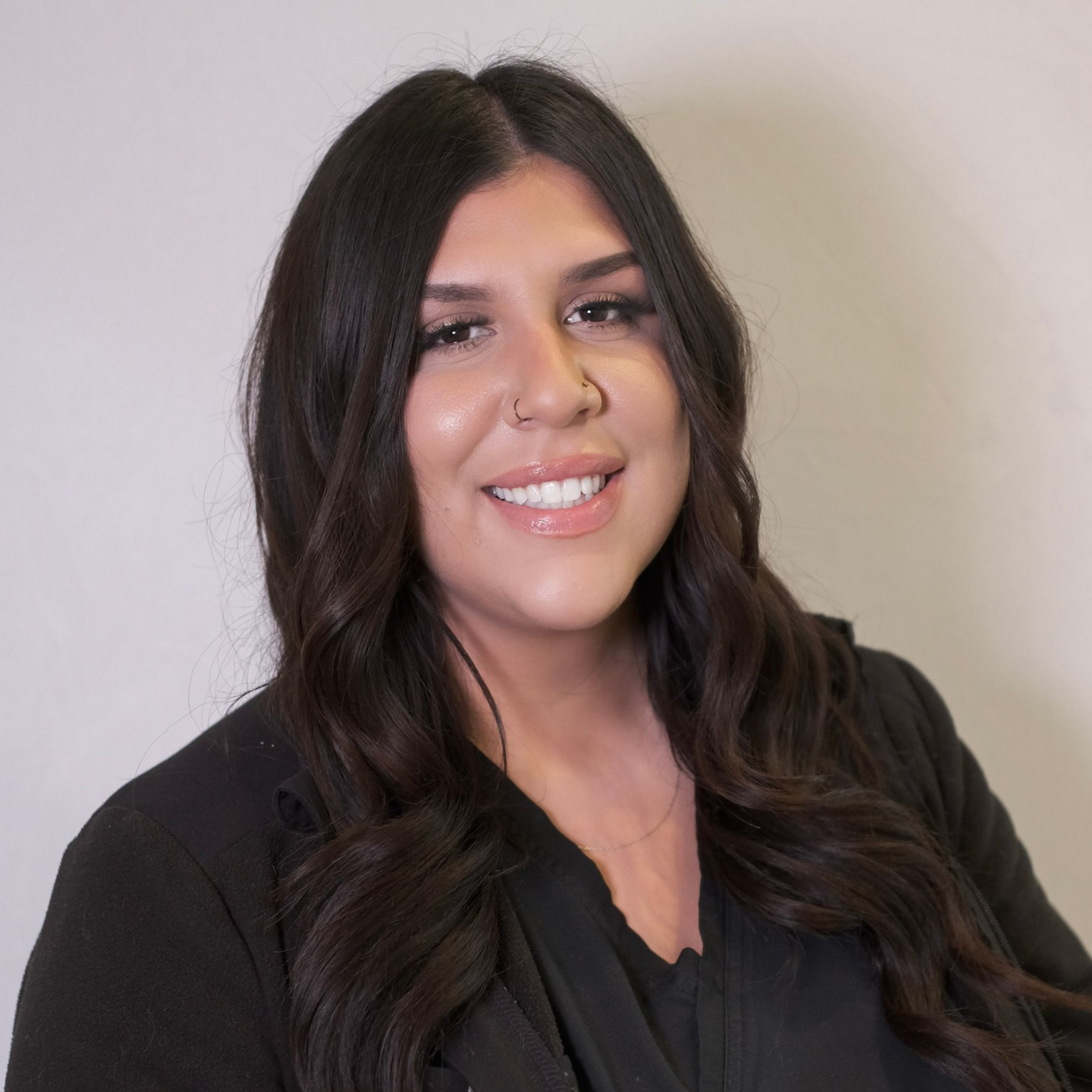 Smiling woman in a black outfit seated on a chair against a light background