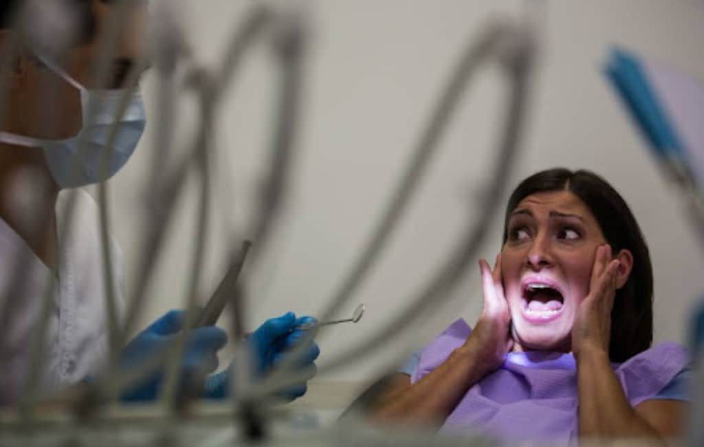 Patient with mouth open in a dental chair, looking startled as a dentist works nearby