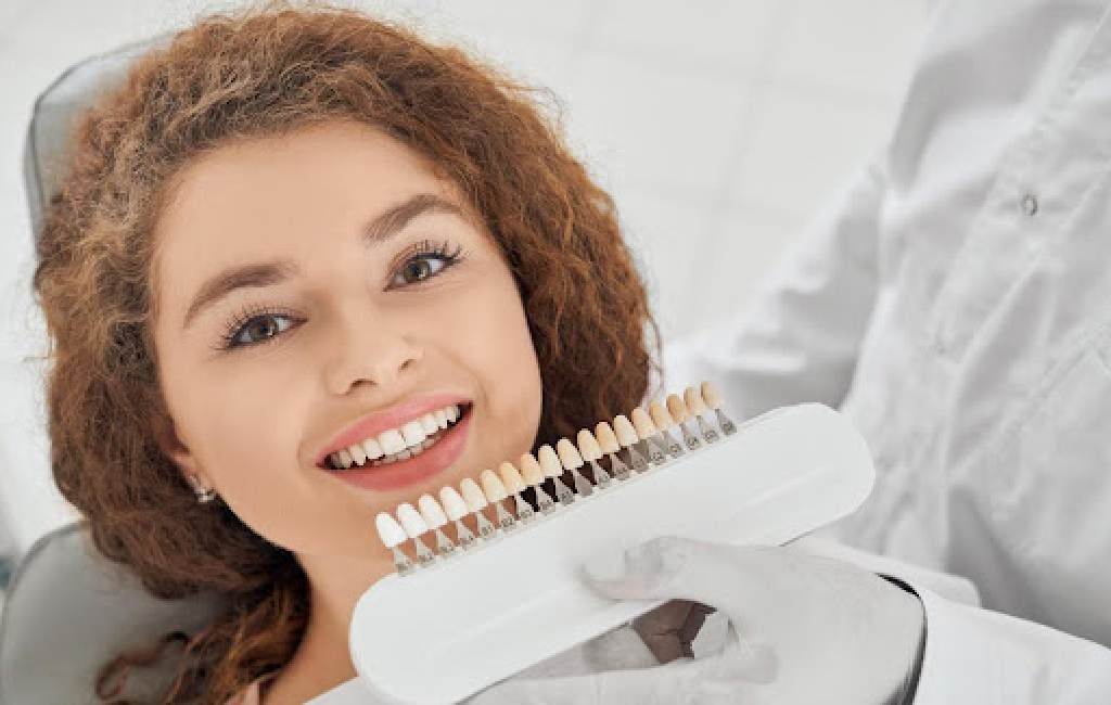 Smiling dental patient holding a teeth shade guide during a dental exam