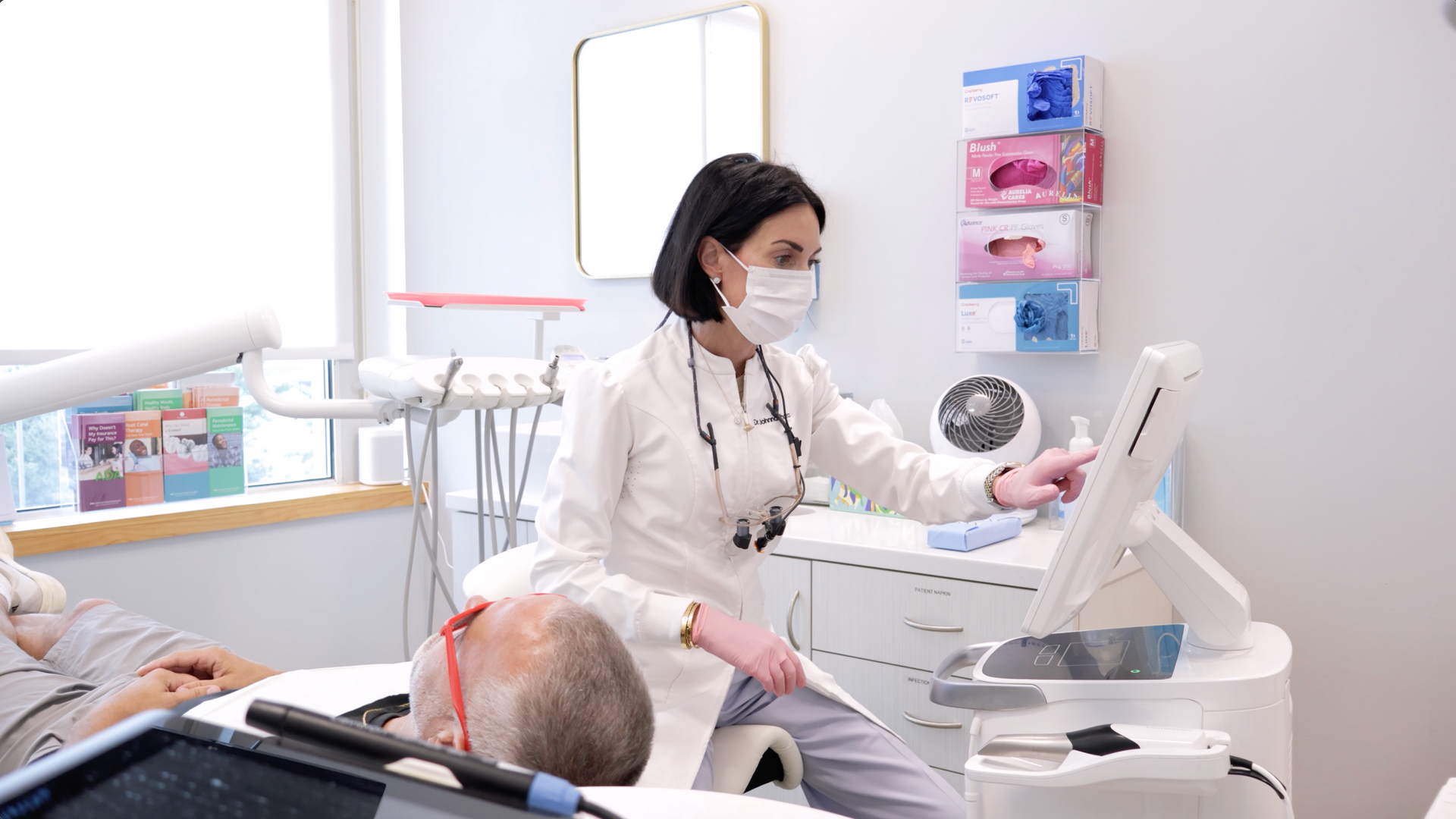 Dental patient smiling during a checkup while a dentist in a mask assists in a bright clinic