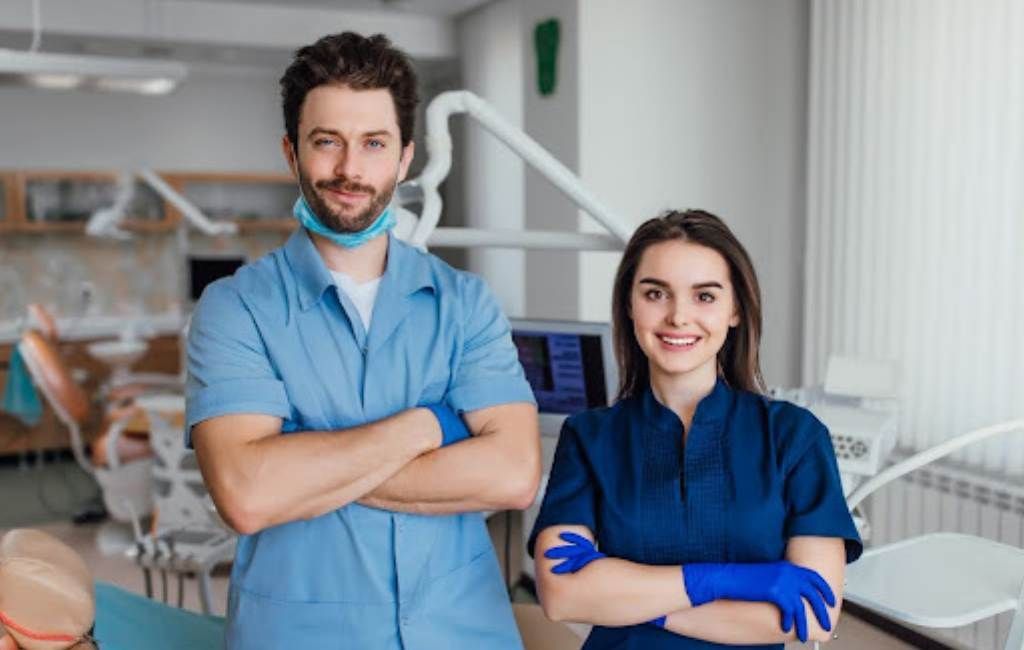 Two dental professionals in blue scrubs standing with arms crossed in a modern clinic