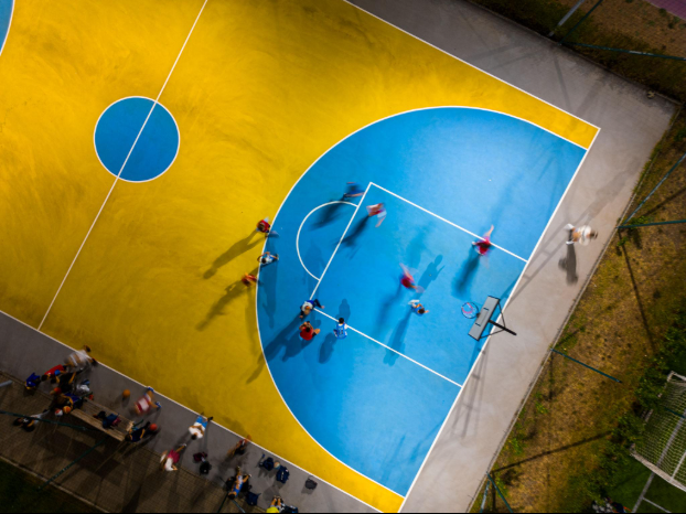 “Aerial view of a bright yellow and blue basketball court with players during a court builder service in Tucson, AZ”