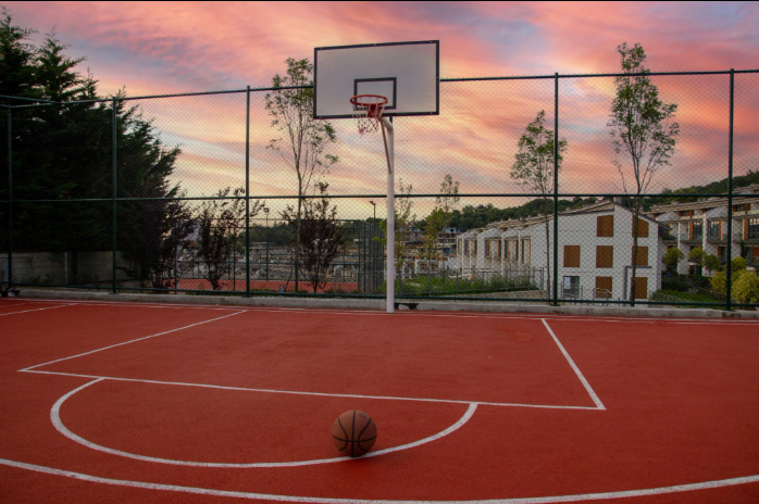 “Outdoor red basketball court with a hoop, white lines, and sunset sky after a court builder service in Tucson, AZ”