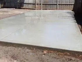 A large concrete slab is sitting in the dirt in front of a fence. A large concrete slab is sitting in the dirt in front of a fence.
