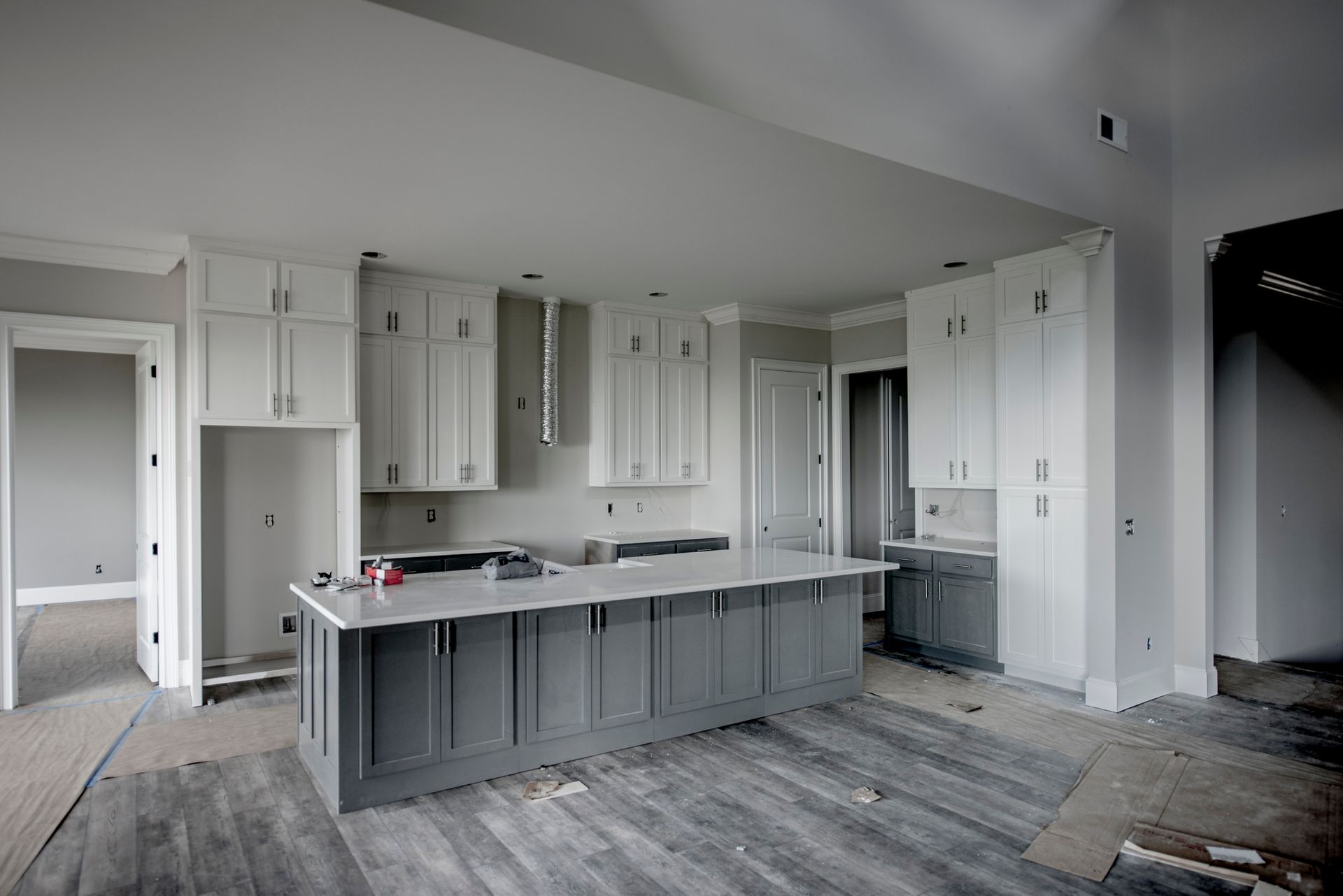 Kitchen under construction with gray island, white cabinets, and light wood-look flooring.