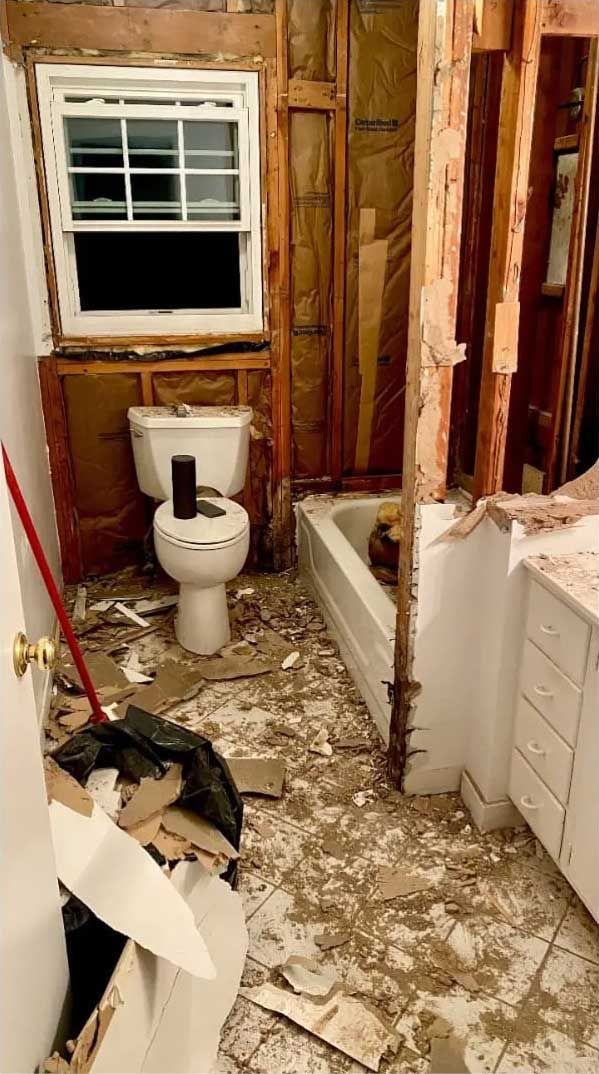 Bathroom renovation in progress, toilet and bathtub visible. Demolition debris on floor; exposed wall studs.