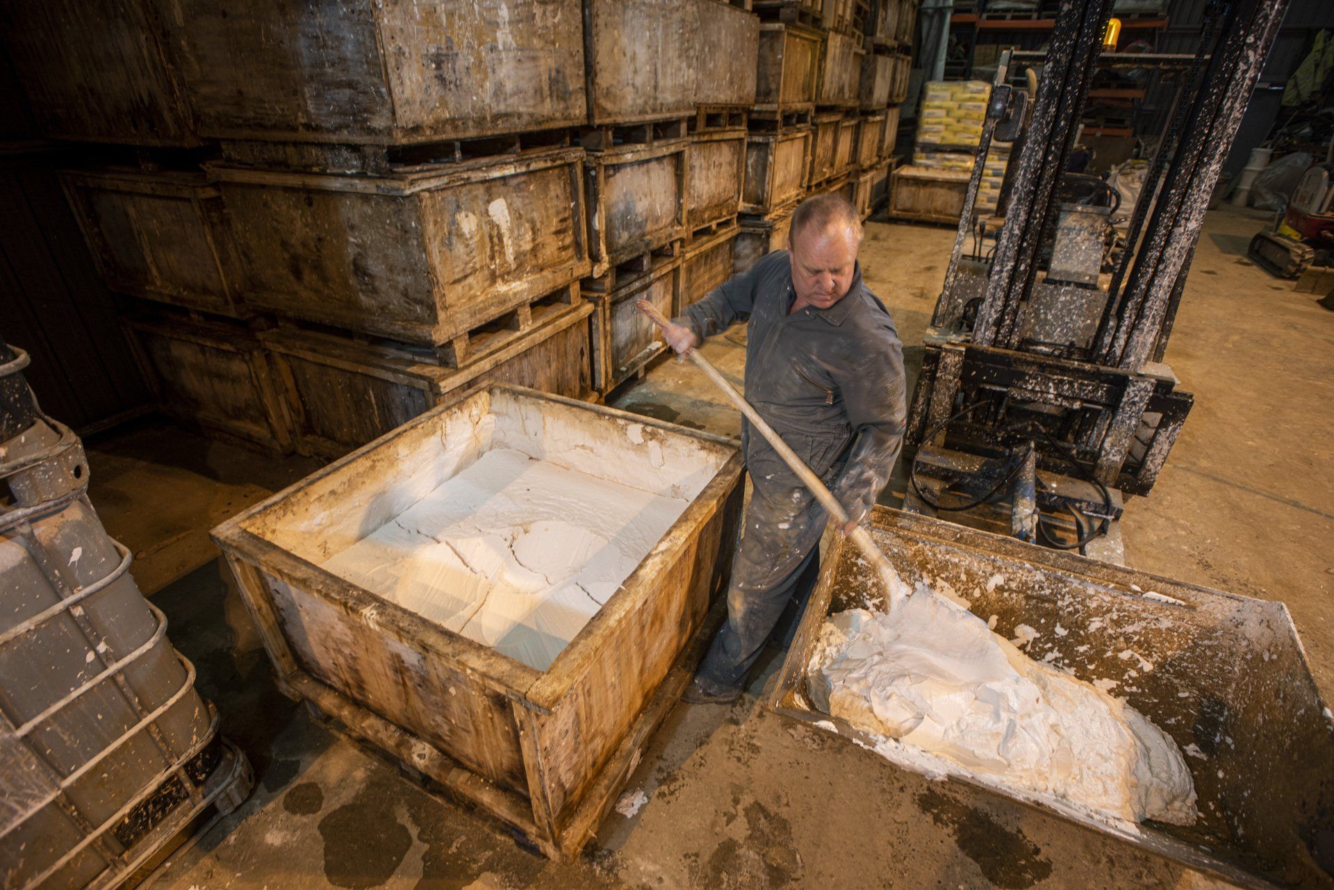 A man is working in a warehouse with a shovel and a forklift.