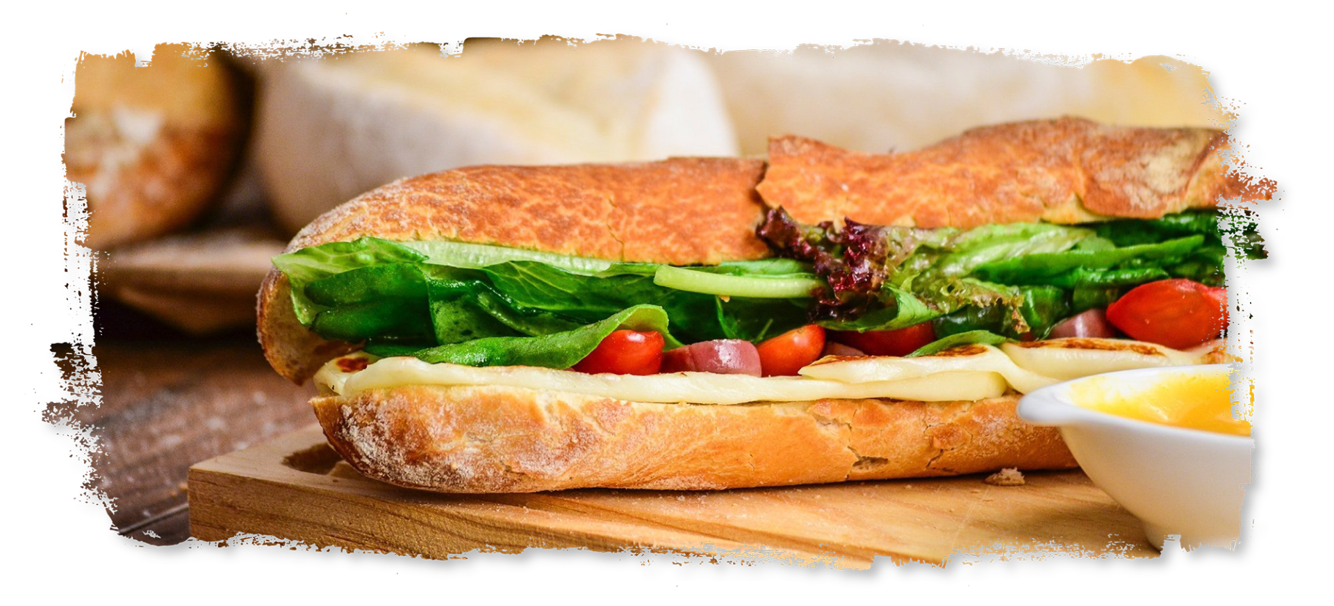 A sandwich is sitting on a wooden cutting board next to a bowl of butter.