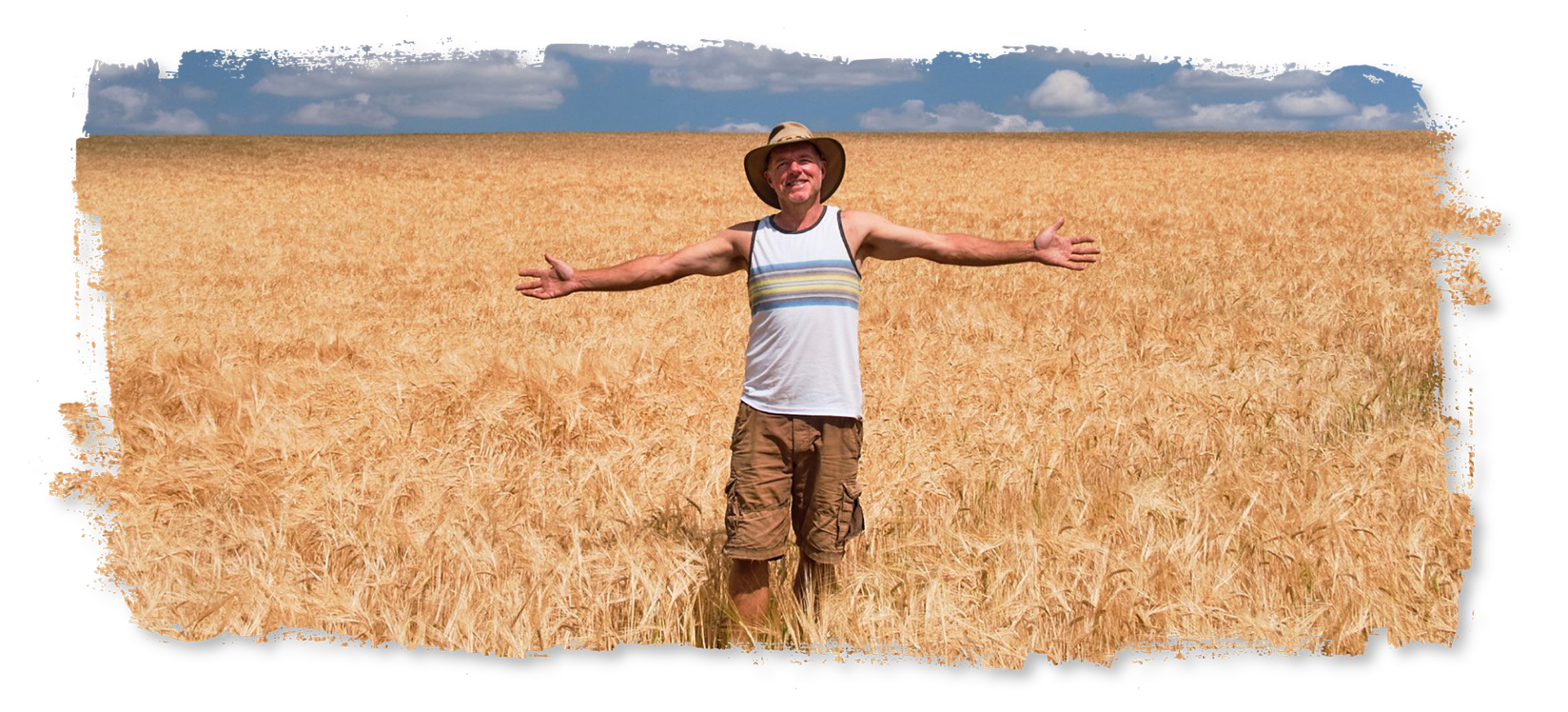 A man is standing in a field of wheat with his arms outstretched.
