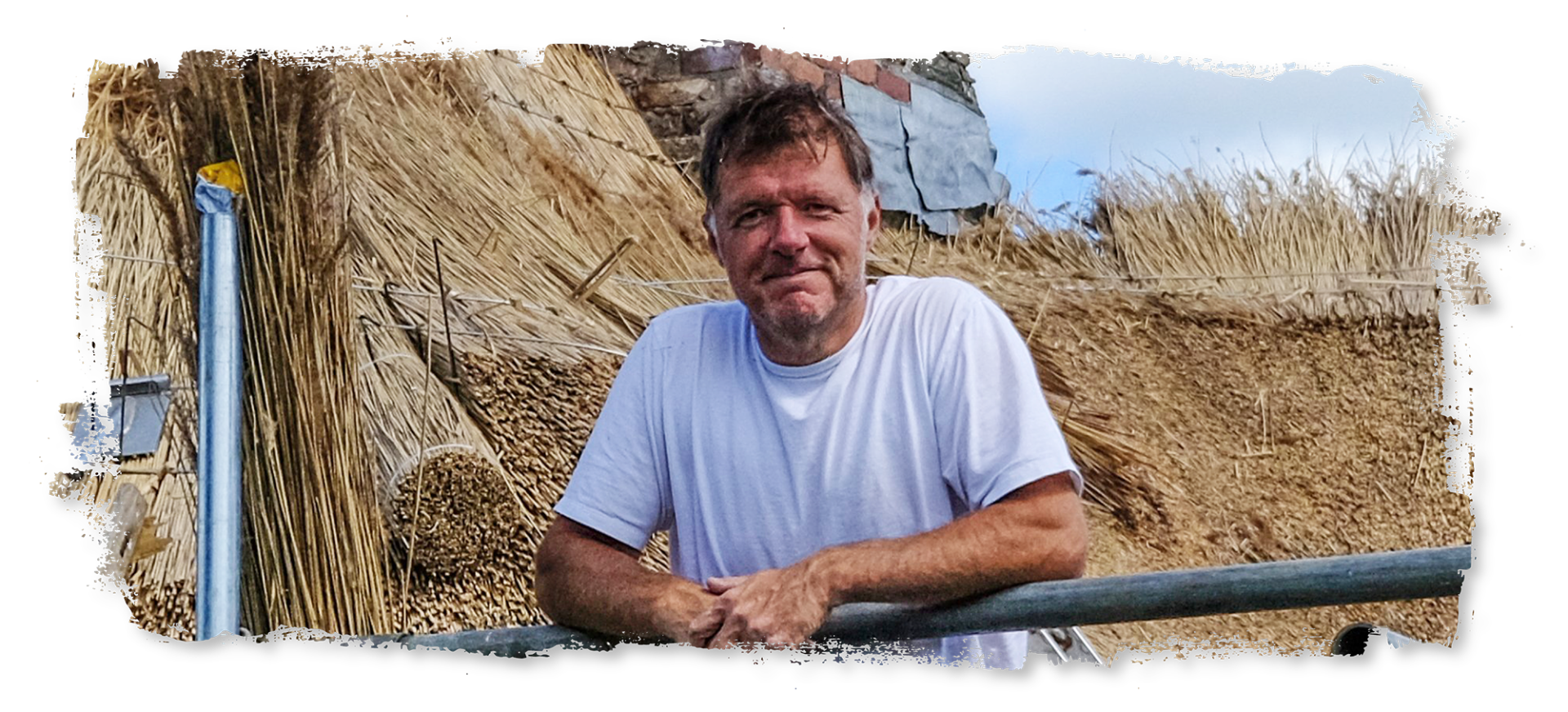 A man in a white shirt is standing in front of a pile of hay.