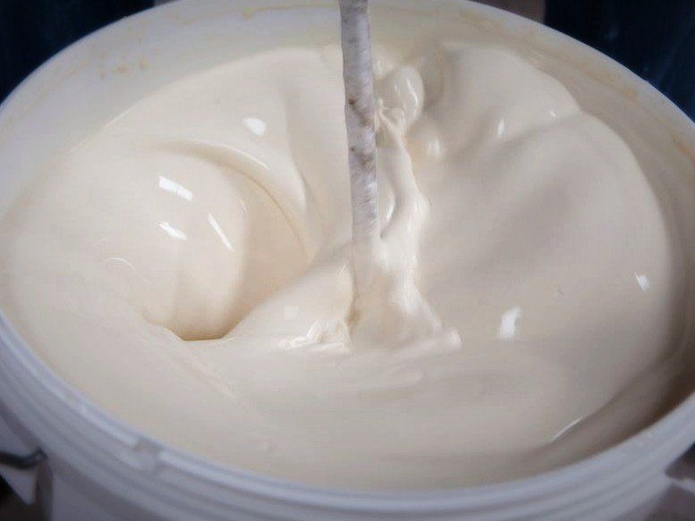 A bucket of white liquid is being stirred with a stick.