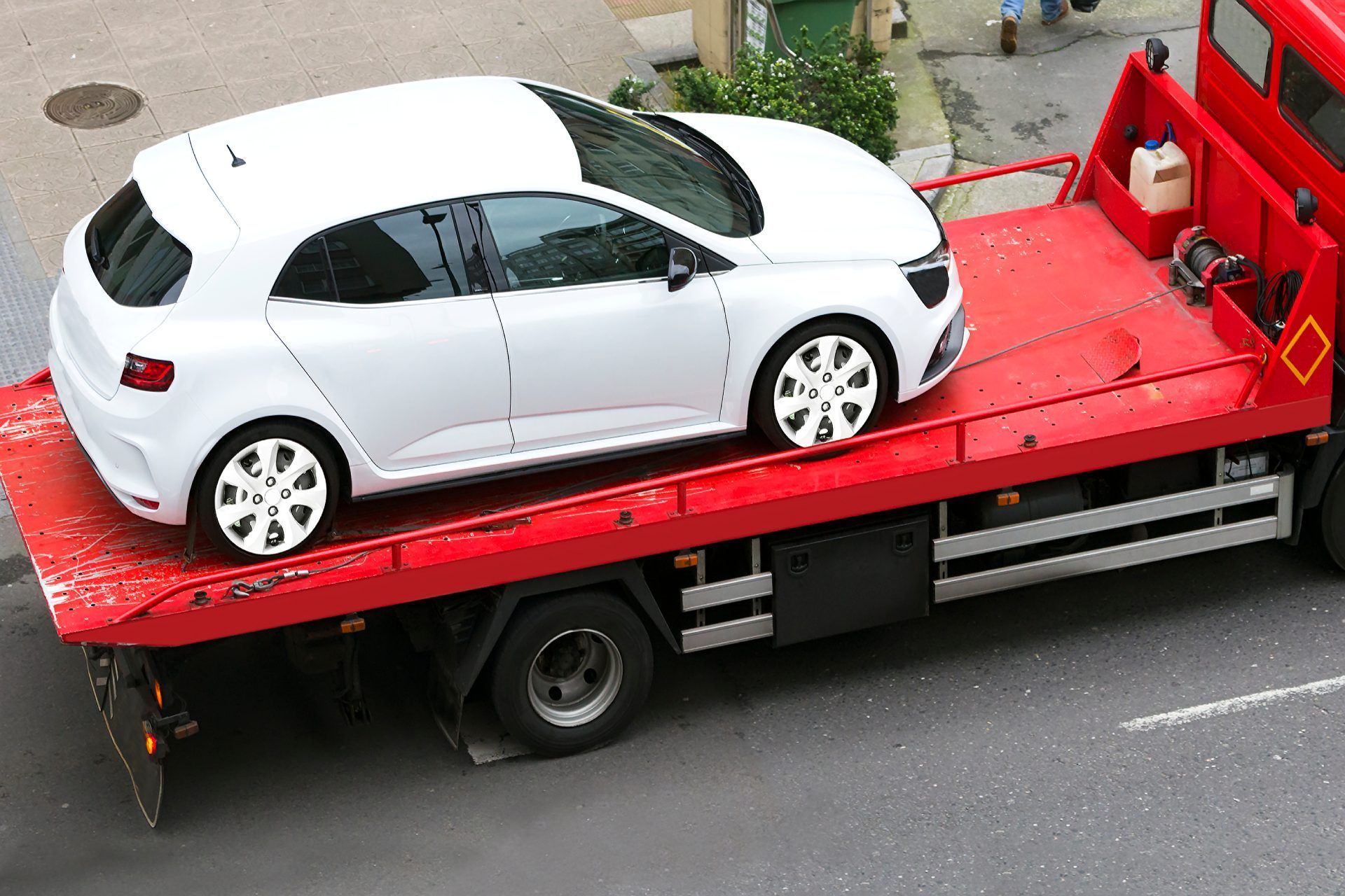 White car on red tow truck, on a street.