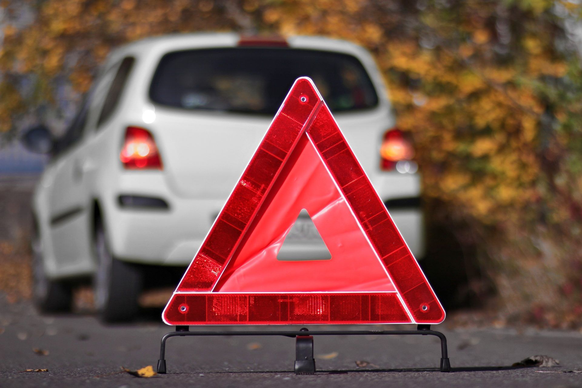 Red warning triangle on road in front of a white car with taillights on.