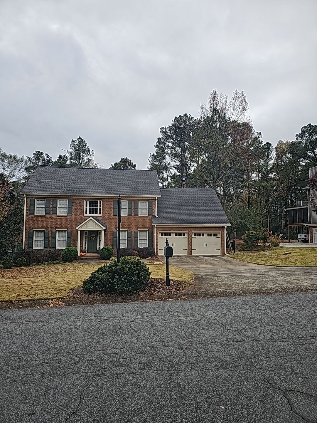 Two-story brick house with a two-car garage, gray shingles, and beige garage doors on a cloudy day.