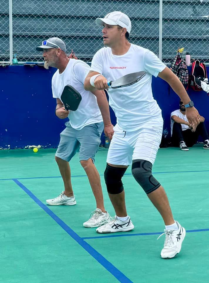 Two men are playing tennis on a green court  at the Playa Del Carmen Pickleball Club in Playa Del Carmen, Mexico 