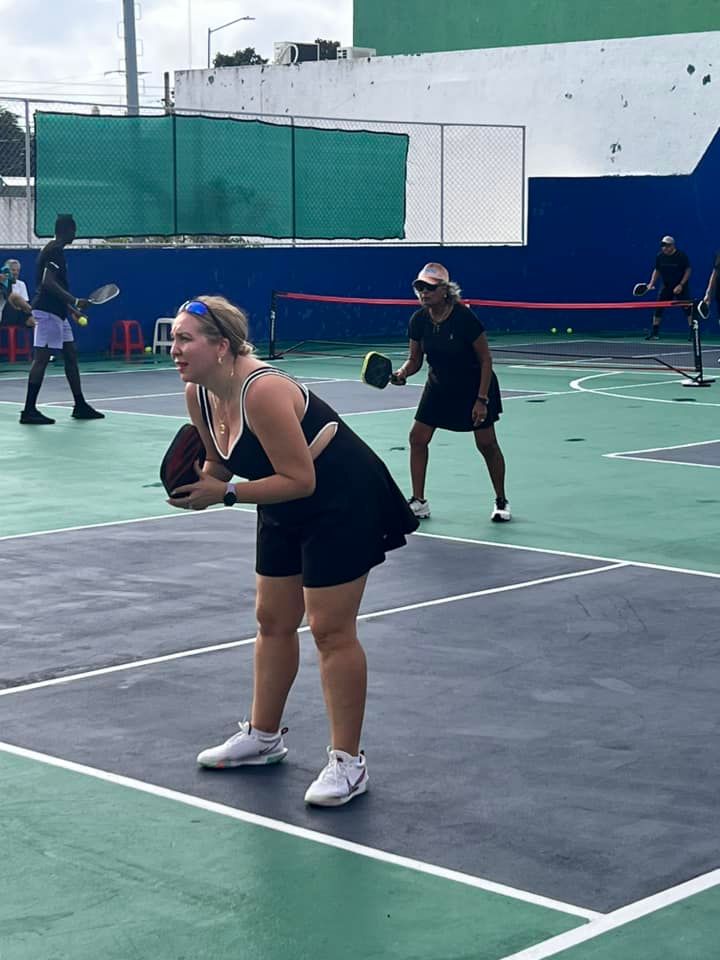 A man is standing on a pickleball court holding a red picklebal paddle  at the Playa Del Carmen Pickleball Club in Playa Del Carmen, Mexico rackets.