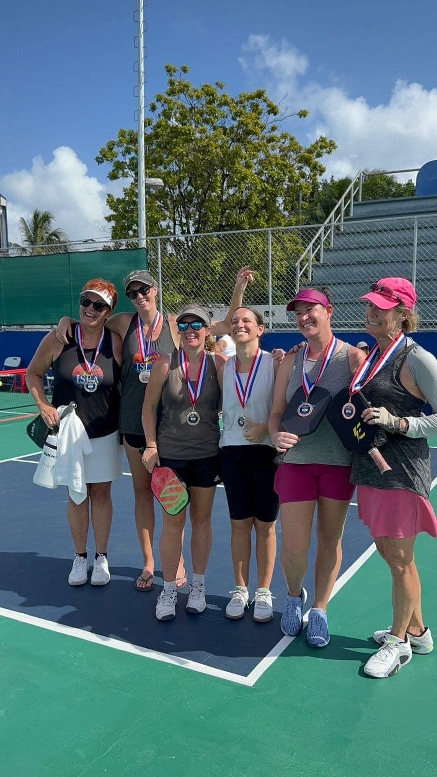 A group of women are posing for a picture on a pickleball court. at the Playa Del Carmen Pickleball Club in Playa Del Carmen, Mexico rackets.