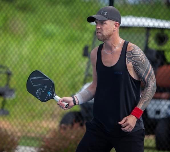 A man is walking on a pickleball court holding a paddle that says quadram  at the Playa Del Carmen Pickleball Club in Playa Del Carmen, Mexico rackets.