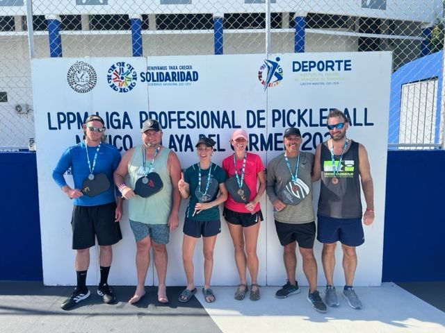 A group of pickleball players standing in front of a wall at the Playa Del Carmen Pickleball Club in Playa Del Carmen, Mexico rackets.