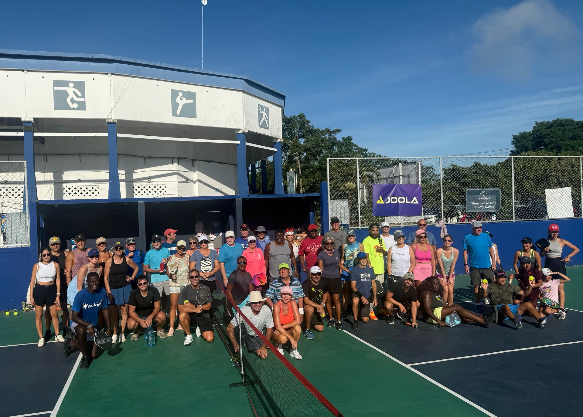 A group of people posing for a picture on a pickleball court  at the Playa Del Carmen Pickleball Club in Playa Del Carmen, Mexico rackets.