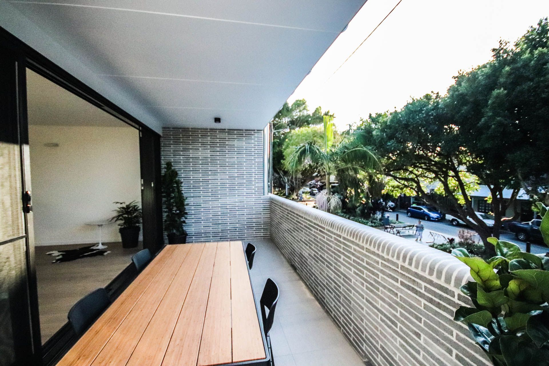 Balcony with wooden table, overlooking a street with trees. Indoor space visible through sliding door— Ray Smith Electrical in Korora, NSW