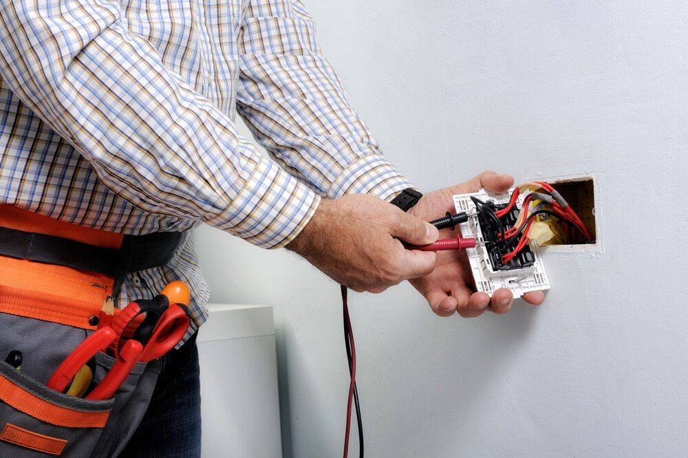 An Electrician is Installing a Light Switch on a Wall — Ray Smith Electrical in Korora, NSW