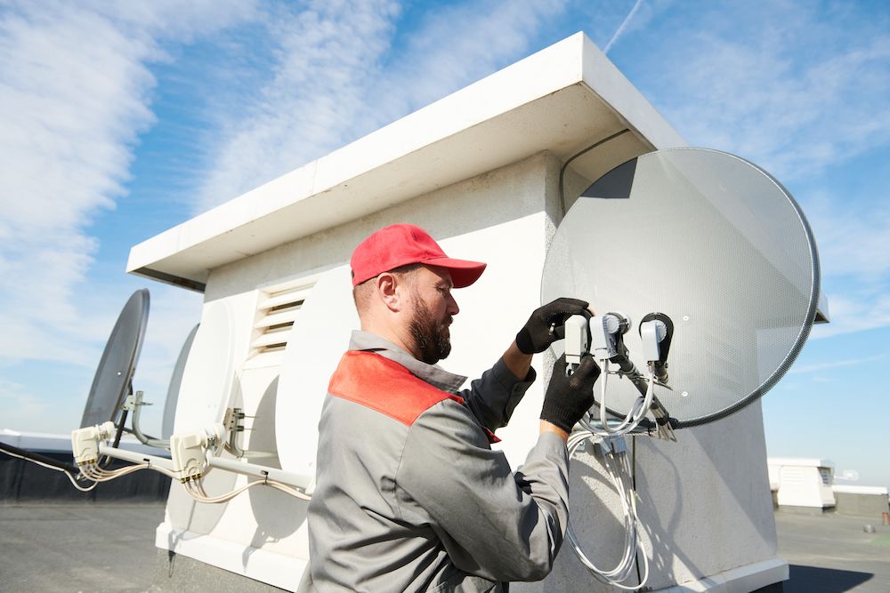 Man in Red Cap and Work Uniform Adjusts Antenna on a Rooftop — Ray Smith Electrical in Korora, NSW