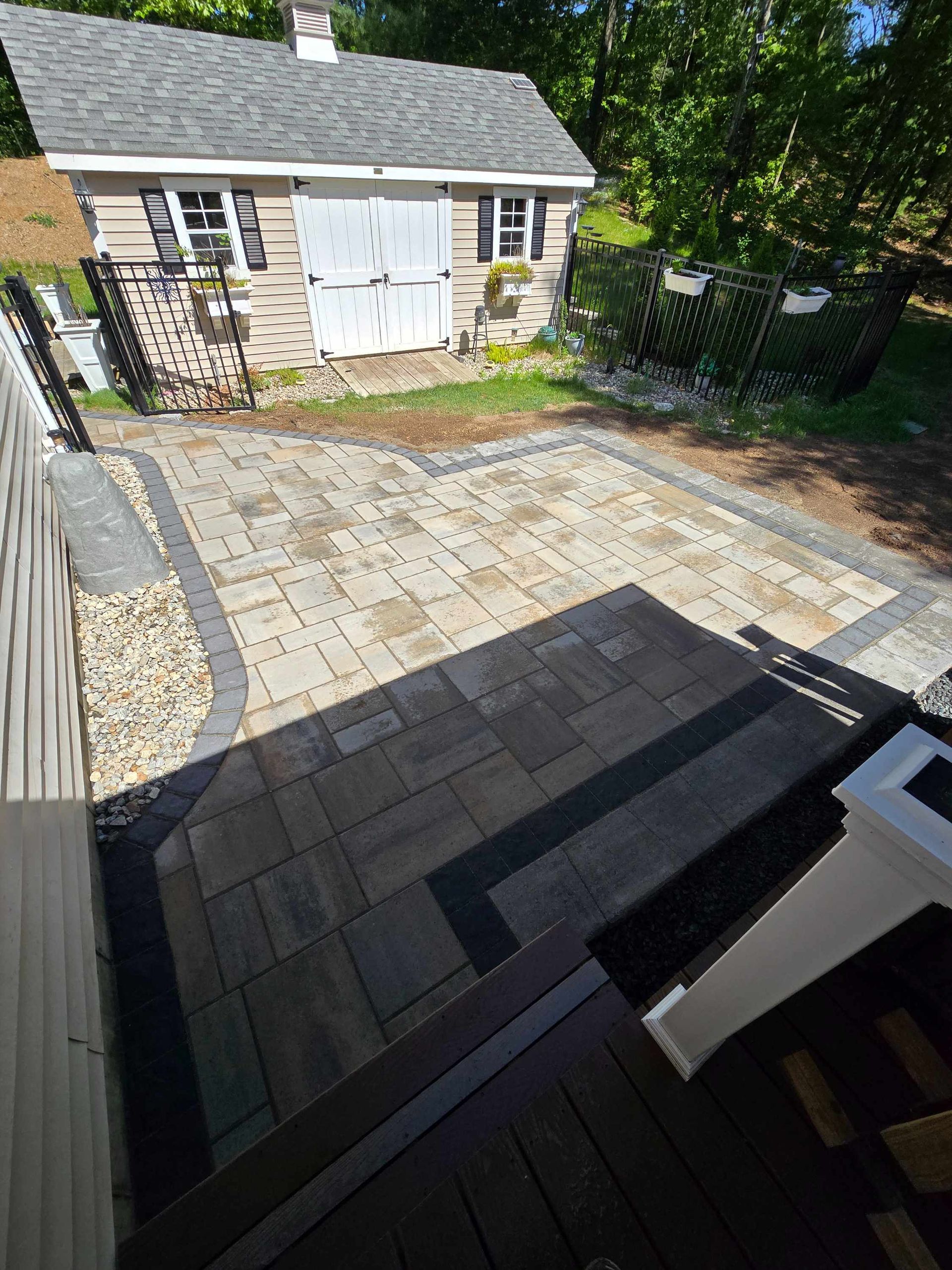A residential backyard shows a freshly dug trench along a marked garden area with a yellow-handled shovel.
