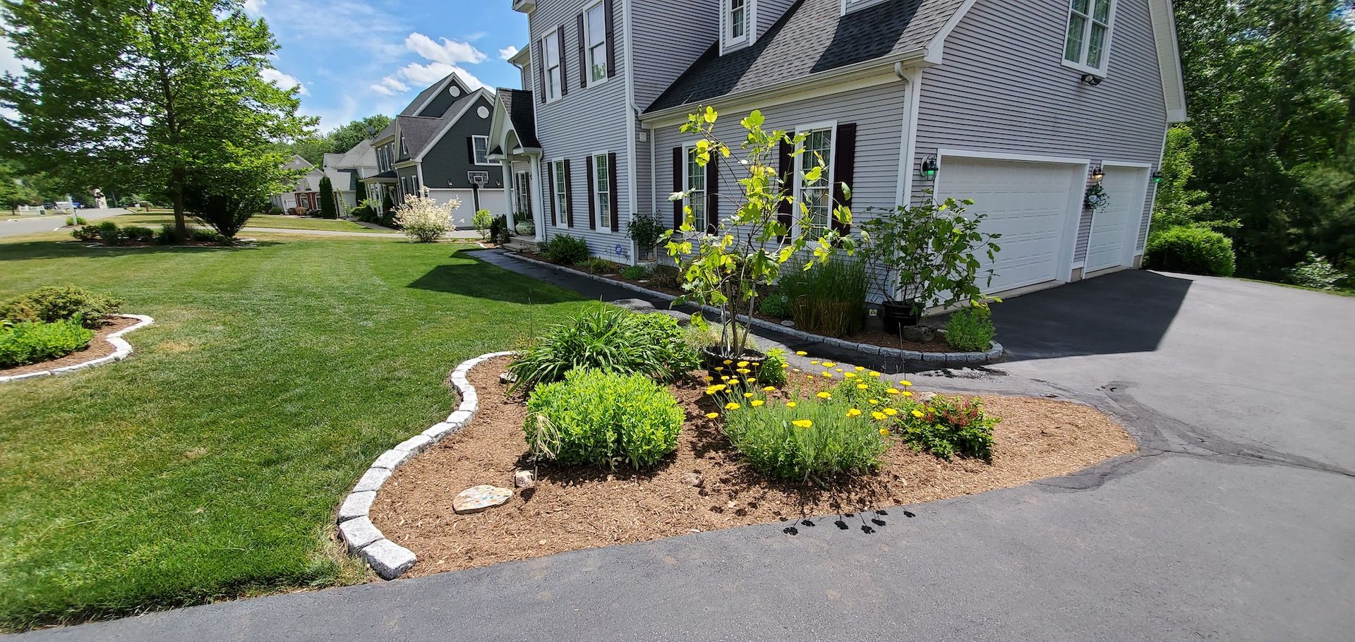 A residential house with a green lawn and a flowerbed lined with bricks. A driveway is on the right.