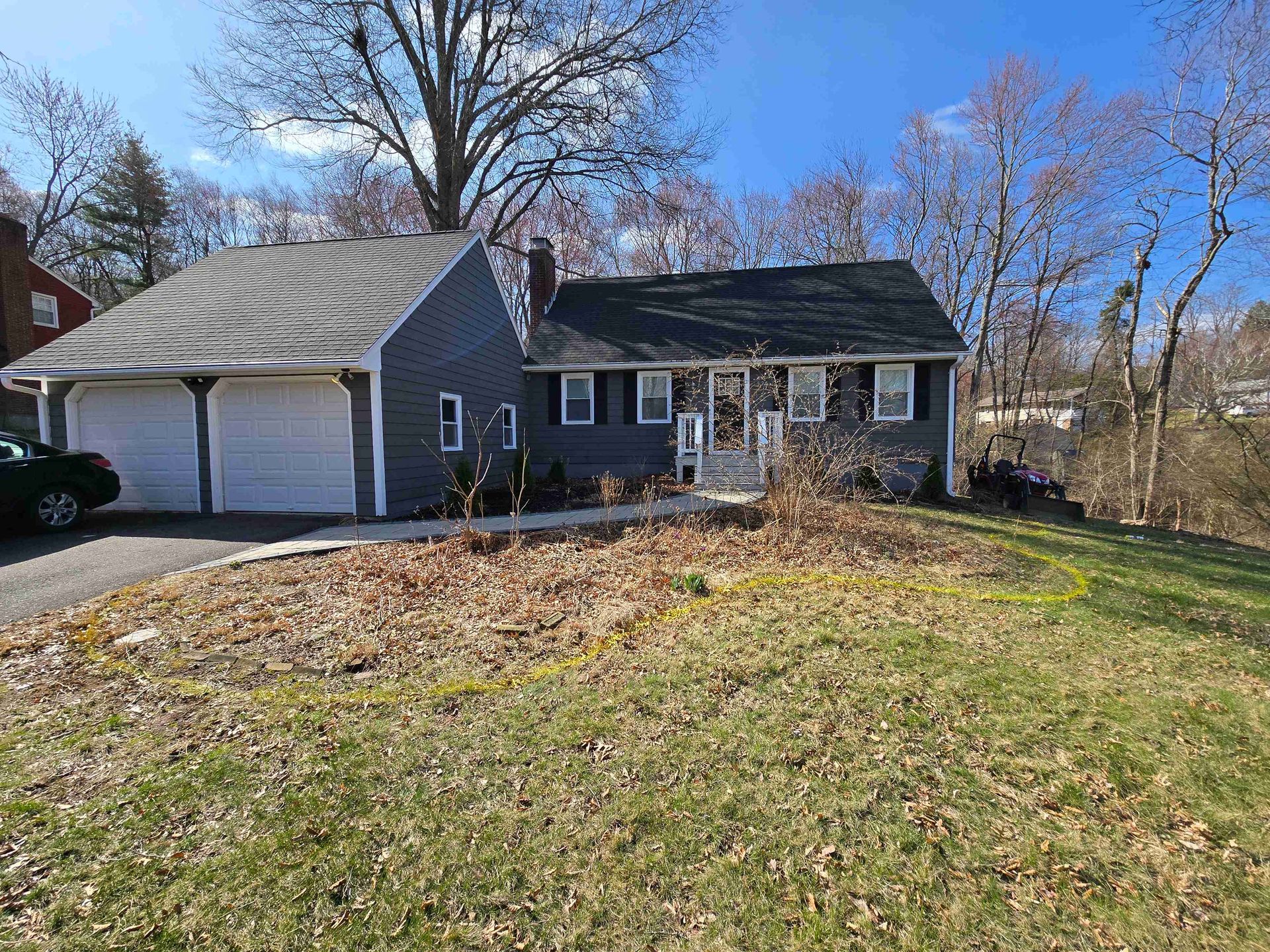 A gray-sided house with an attached two-car garage, dark roof, and a front yard covered in dry, dormant vegetation.