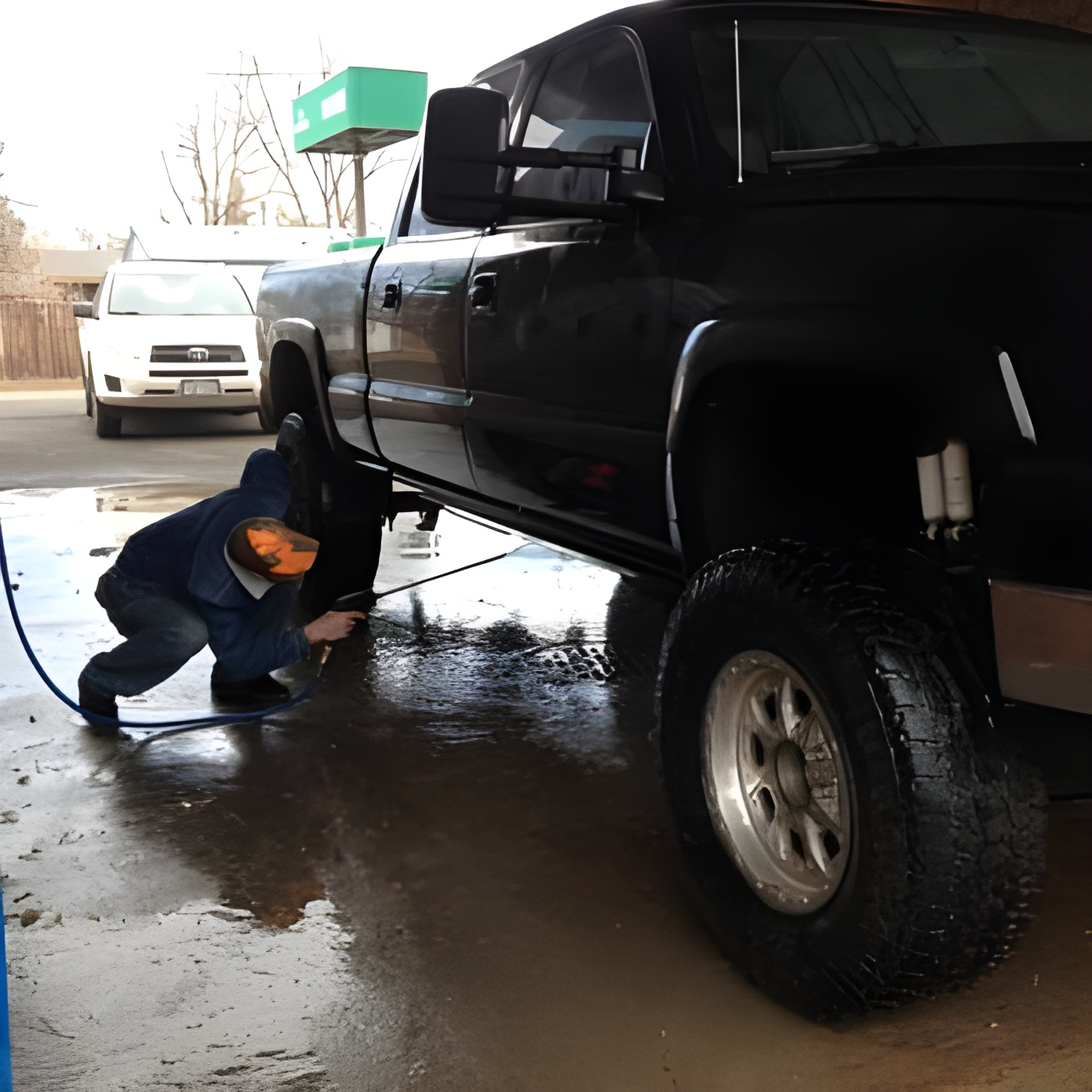Person washing a large black truck at a car wash.